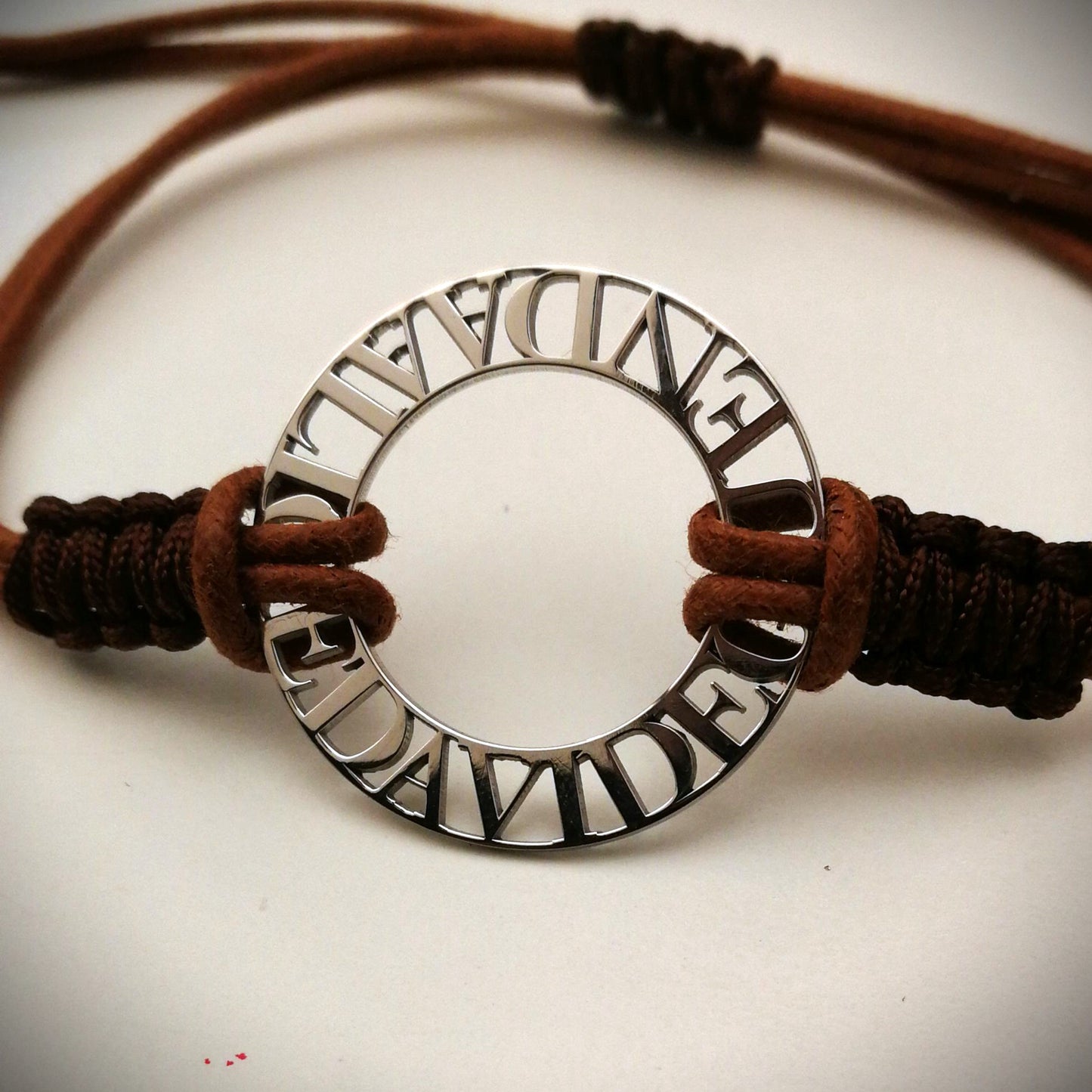 Immagina un cerchio liscio e leggero, con nomi traforati che emergono come piccole sculture tra il vuoto e la luce. Ogni lettera è incisa con precisione, creando un contrasto tra il metallo freddo e il calore del cordino intrecciato a mano, morbido e avvolgente sul polso. La superficie è liscia, con bordi definiti ma delicati al tatto. Questo bracciale personalizzato è un abbraccio in argento, con parole che parlano di affetti, ricordi e connessioni profonde.