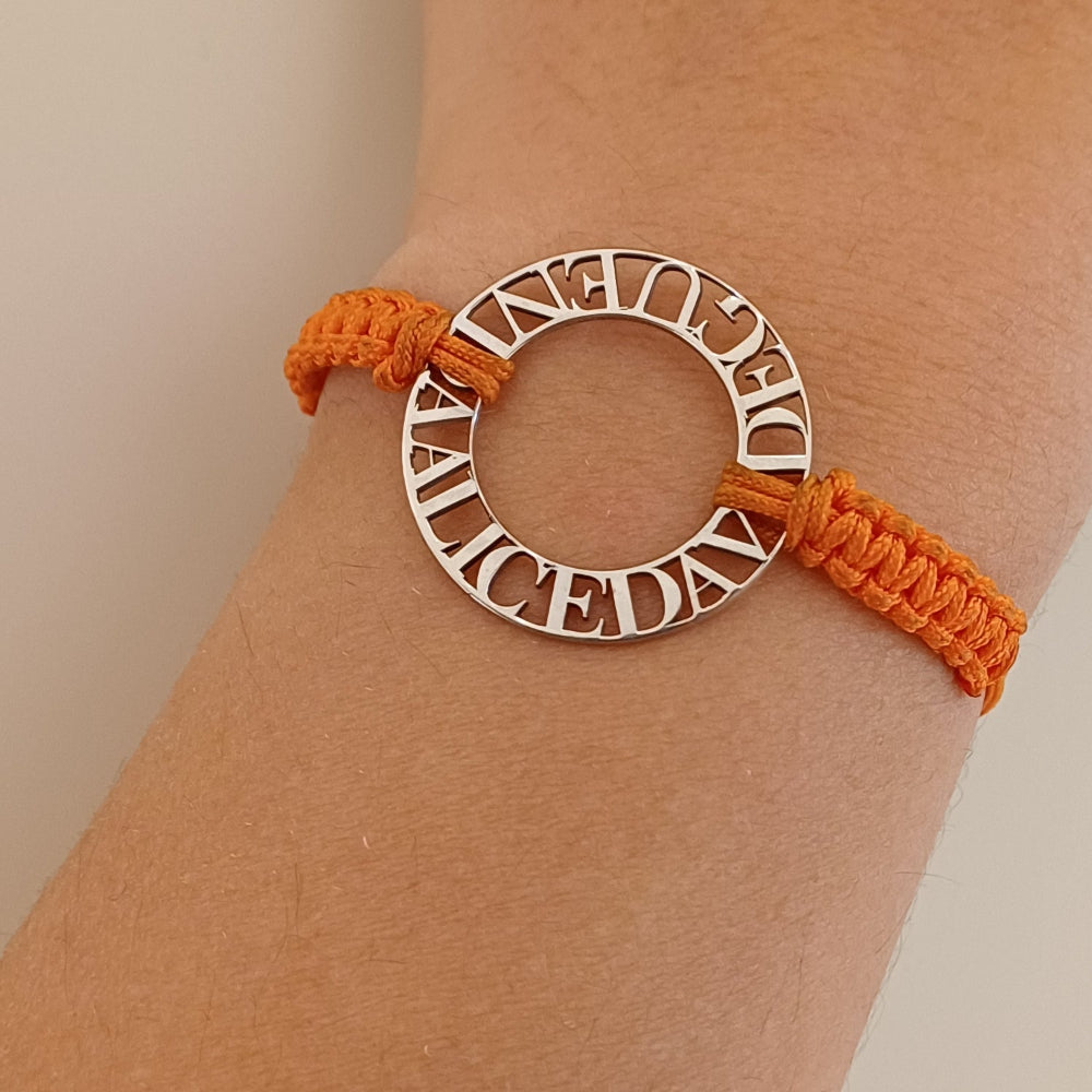 Immagina un cerchio liscio e leggero, con nomi traforati che emergono come piccole sculture tra il vuoto e la luce. Ogni lettera è incisa con precisione, creando un contrasto tra il metallo freddo e il calore del cordino intrecciato a mano, morbido e avvolgente sul polso. La superficie è liscia, con bordi definiti ma delicati al tatto. Questo bracciale personalizzato è un abbraccio in argento, con parole che parlano di affetti, ricordi e connessioni profonde.