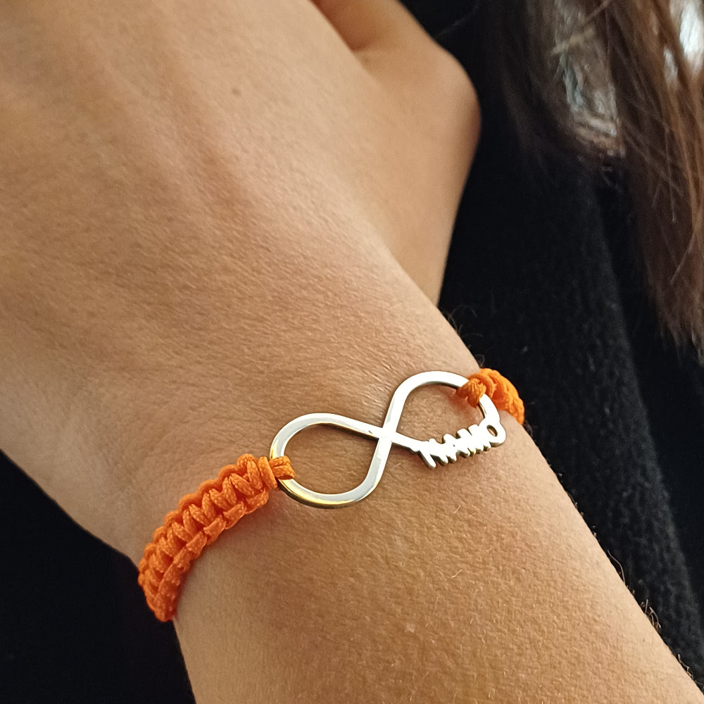 Il bracciale ha un design minimal ed elegante: un simbolo dell'infinito in argento 925 dal profilo liscio e brillante. Su un lato del simbolo, la scritta "Ti Amo" è delicatamente intagliata. Il bracciale è legato con un laccio in corda arancione intrecciata, che aggiunge un tocco vivace. Il contrasto tra il metallo freddo e la texture morbida del laccio lo rende piacevole da indossare, leggero ma resistente. Perfetto per chi ama i gioielli slim e personalizzati.Bracciale Infinito Ti Amo indossato dettaglio