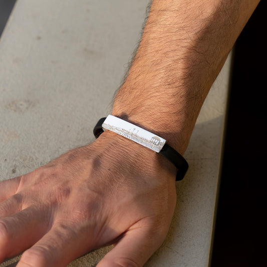 Bracciale in argento 925 e caucciù nero, con targa rettangolare lunga 45 mm e alta 10 mm. La superficie è incisa con il paesaggio della Terrazza Mascagni, simbolo di Livorno. Il caucciù è comodo al polso. Perfetto per chi ama il mare, la città o vuole un gioiello artigianale e ricco di significato.