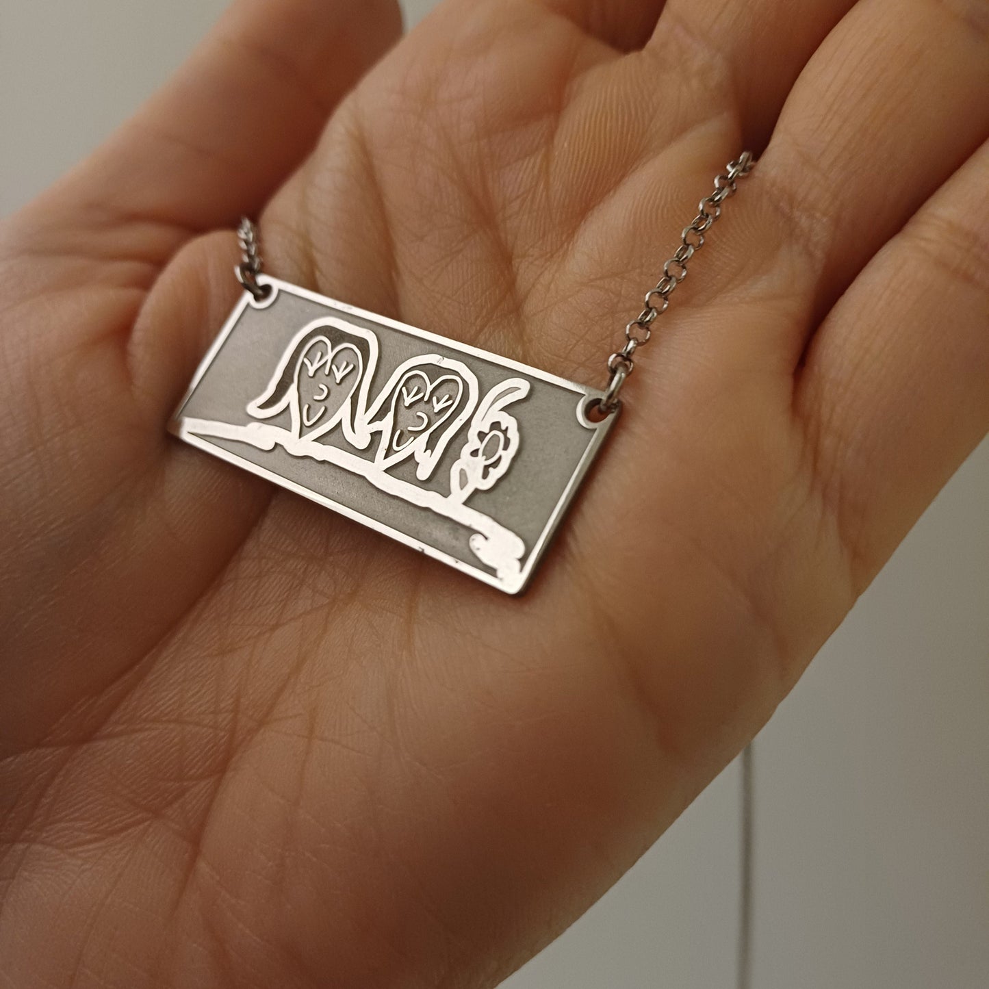 Girocollo in argento 925, con catena fine e leggera.
Al centro pende una targhetta piatta e lucida, grande circa 2,5 cm, di forma rettangolare.
Sulla superficie è inciso il disegno di un bambino, spesso fatto a mano su carta e poi fedelmente riportato sul metallo.
Il bordo è morbido e leggermente stondato, il tutto è liscio al tatto.
Il girocollo è leggero, con chiusura semplice e sicura. Si porta vicino al cuore.