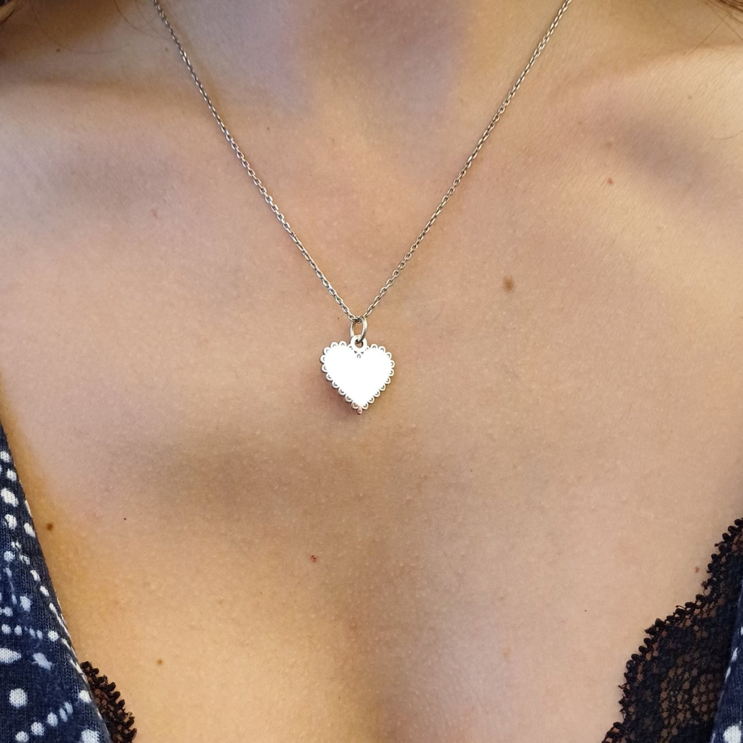 Questo ciondolo a forma di cuore è in oro, liscio al centro con una cornice ricamata che aggiunge una sensazione delicata al tatto. Il bordo è decorato con piccoli archi che ricordano una serie di petali, donando una consistenza morbida e piacevole sotto le dita. Al tatto è leggero ma resistente, trasmettendo un senso di eleganza e cura artigianale. La sua forma è semplice ma raffinata, perfetta per chi ama gioielli discreti e raffinati.