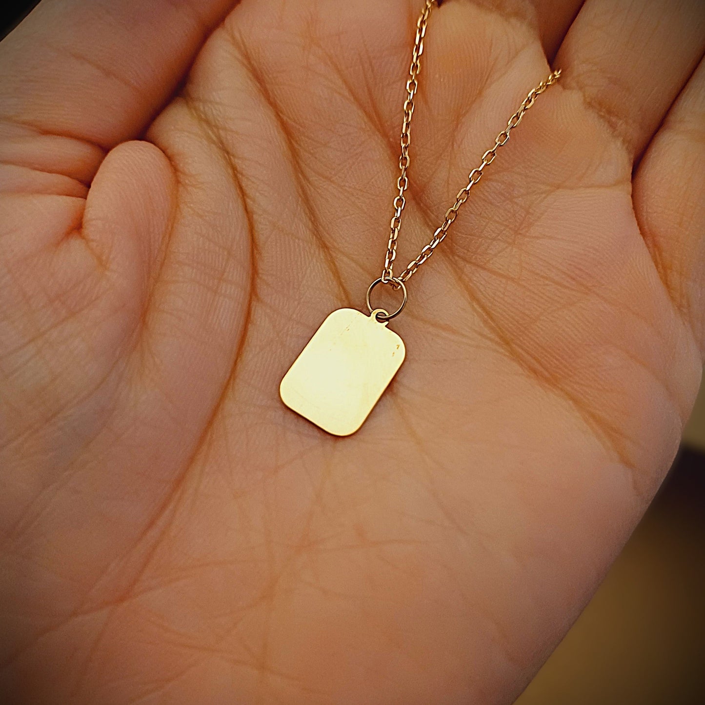 Questo ciondolo ha la forma di un rettangolo dai bordi morbidi, misura 15 millimetri in altezza ed è disponibile in oro 750 o argento 925. La superficie è liscia e lucida, piacevole al tatto. È pensata per essere personalizzata con un’incisione, come un nome, una data o una parola speciale. È leggera e realizzata a mano nel nostro laboratorio artigianale, con cura e attenzione per ogni dettaglio.