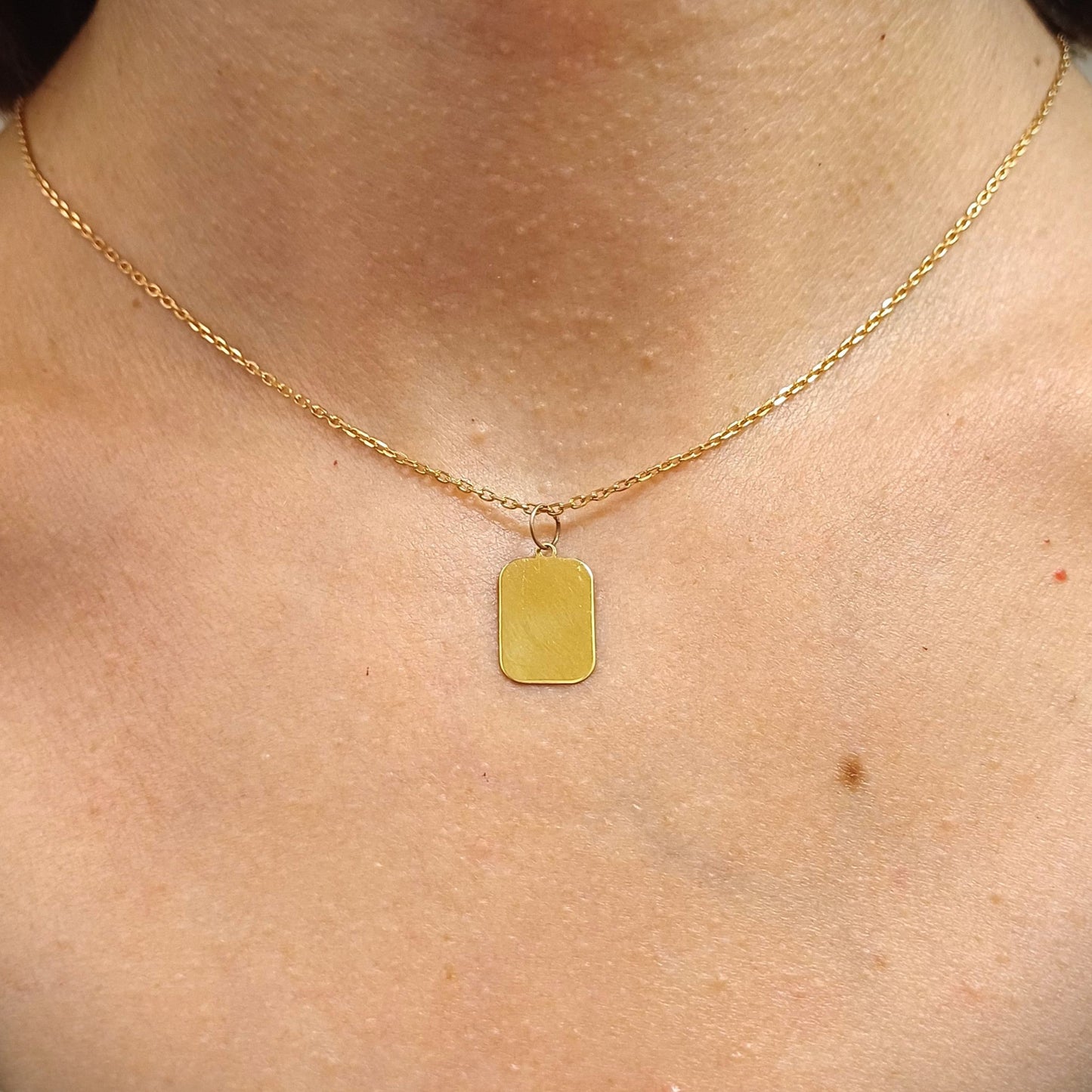 Questo ciondolo ha la forma di un rettangolo dai bordi morbidi, misura 15 millimetri in altezza ed è disponibile in oro 750 o argento 925. La superficie è liscia e lucida, piacevole al tatto. È pensata per essere personalizzata con un’incisione, come un nome, una data o una parola speciale. È leggera e realizzata a mano nel nostro laboratorio artigianale, con cura e attenzione per ogni dettaglio.