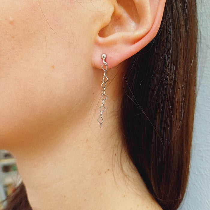 Questi orecchini pendenti sono realizzati in argento 925 nelle varianti Rodiato, Dorato e Ramato e presentano una catena leggera formata da piccoli cuori vuoti collegati tra loro. Il design è arioso e delicato, con una cascata sottile che ondeggia dolcemente con ogni movimento. La chiusura è a perno con farfallina, pratica e sicura. Il colore è un caldo oro giallo lucido, che riflette la luce in modo raffinato. Perfetti per chi ama i dettagli romantici e sofisticati.