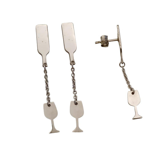 Questi orecchini pendenti in argento 925 sono composti da due elementi collegati da una sottile catenella. La parte superiore rappresenta il collo di una bottiglia, mentre il ciondolo inferiore raffigura un calice da vino inclinato, come se stesse versando il suo contenuto. Alcune versioni presentano una smaltatura a caldo in un intenso colore rosso vino. La superficie è incisa al laser, con dettagli ben definiti. Leggeri e lunghi 5 cm, si muovono delicatamente seguendo i movimenti del viso.