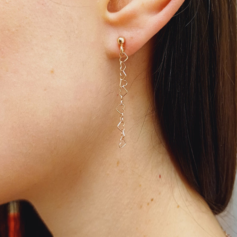 Questi orecchini pendenti sono realizzati in argento 925 nelle varianti Rodiato, Dorato e Ramato e presentano una catena leggera formata da piccoli cuori vuoti collegati tra loro. Il design è arioso e delicato, con una cascata sottile che ondeggia dolcemente con ogni movimento. La chiusura è a perno con farfallina, pratica e sicura. Il colore è un caldo oro giallo lucido, che riflette la luce in modo raffinato. Perfetti per chi ama i dettagli romantici e sofisticati.