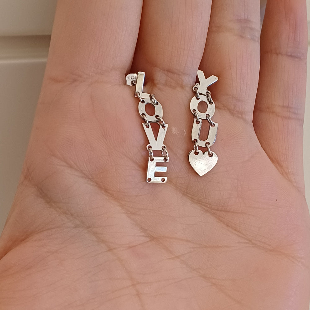 Gli orecchini sono pendenti e mobili, composti da lettere snodabili che formano la scritta "I LOVE YOU". Sono realizzati in argento liscio e brillante, con un design elegante e leggero. Grazie ai piccoli snodi tra le lettere, si muovono delicatamente ad ogni passo, creando un effetto dinamico e raffinato. Perfetti per chi ama gioielli con significato, esprimono un messaggio romantico e universale, da indossare con leggerezza e stile.