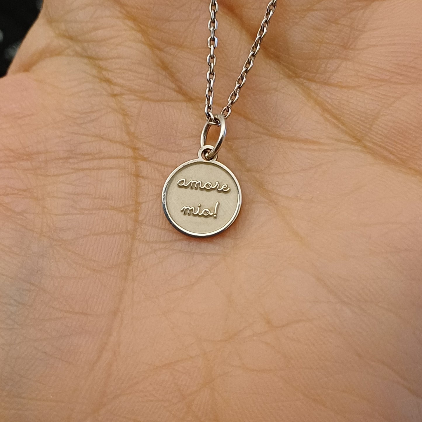 Medaglia tonda in argento, diametro 10 millimetri, con superficie liscia o satinata. Sul fronte è presente la scritta “amore mio” incisa in rilievo delicato. Il bordo è sottile, regolare, piacevole al tatto. Il retro è piatto e incidibile, ideale per aggiungere una frase o una data. Leggera, dal tocco freddo e morbido, da portare al collo o al polso. Un oggetto prezioso dal significato emotivo, fatto completamente a mano.