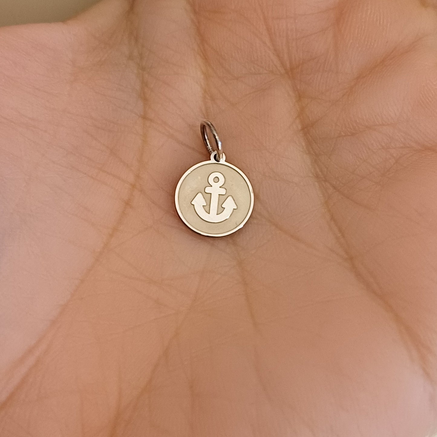 Piccola medaglia tonda in argento 925, diametro 10 millimetri. La superficie è liscia o satinata al tatto, e al centro si avverte una piccola ancora in rilievo: linee morbide, simbolo marino ben riconoscibile. Il bordo è sottile e regolare. Il retro è liscio, pensato per essere inciso con una frase, un nome o una data. L’oggetto è leggero, compatto, dal tocco freddo ma elegante, interamente realizzato a mano, pensato per custodire un messaggio personale.