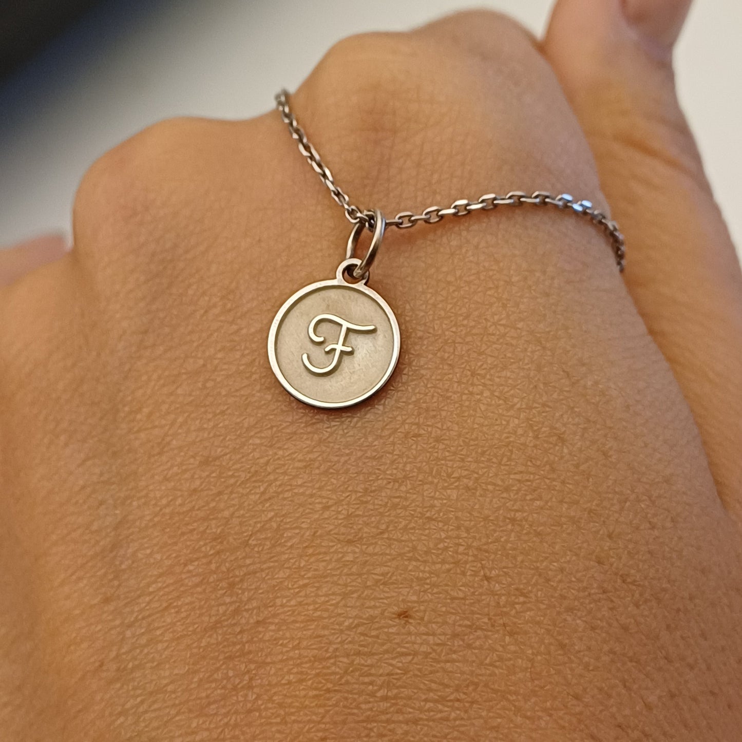 Hai tra le dita una medaglietta tonda in argento 925, dal diametro di circa 1 centimetro. La superficie è morbida al tatto e alterna zone lucide e satinate.
Al centro, in rilievo, si distingue la lettera F con uno stile elegante e sinuoso.
Sul retro si può incidere un nome o una dedica.
È leggera, raffinata e fatta a mano, perfetta per essere indossata su una catenina o aggiunta a un bracciale.