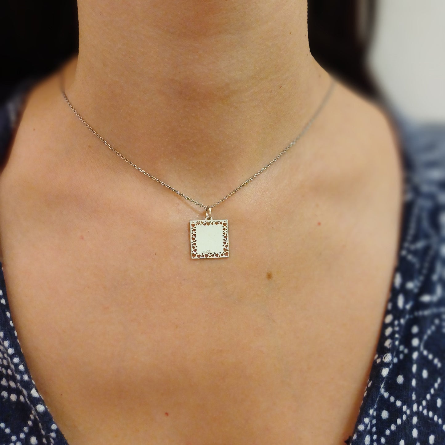 Ciondolo quadrato di 14 mm in argento 925 o oro 750, con bordi traforati da piccoli cuori. La superficie anteriore mostra una medaglia liscia e lucente, il retro è completamente liscio per una personalizzazione con dedica. Perfetto come regalo simbolico per innamorati, può essere indossato su collane, bracciali o charm. Realizzato artigianalmente con materiali anallergici di alta qualità, è un gioiello delicato e resistente, ideale per un legame autentico e duraturo.