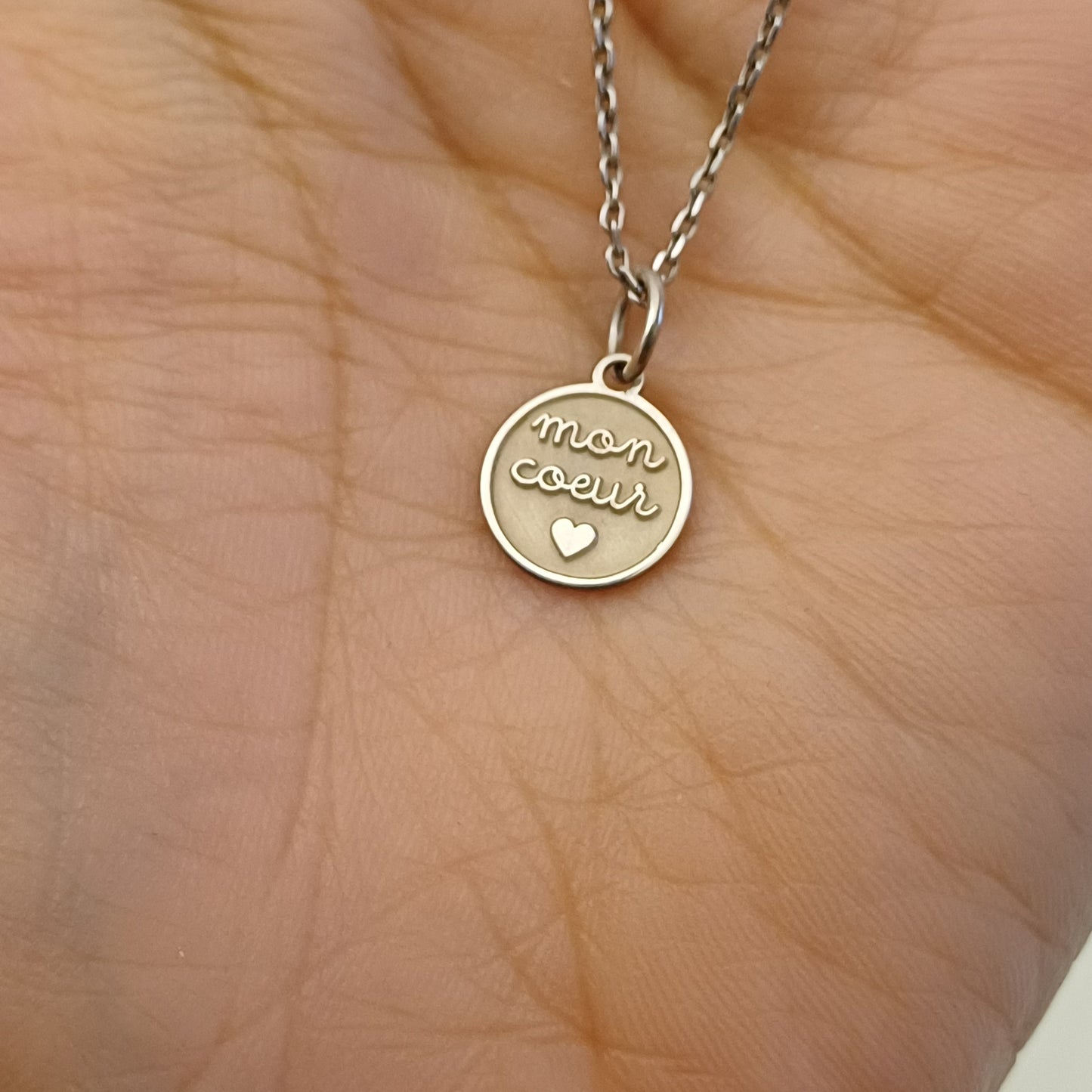 Ciondolo rotondo in argento 925 anallergico, diametro 10 mm. Sul davanti è incisa in rilievo la scritta “mon cœur”, con lettere dolci e rotonde, al centro di una superficie satinata. Sotto le parole è inciso un piccolo cuore pieno. Il bordo è sottile e liscio. Il retro è completamente piatto e può essere personalizzato con una breve incisione. Può essere usato come pendente per collana, bracciale o portachiavi. Leggero, delicato e simbolico.