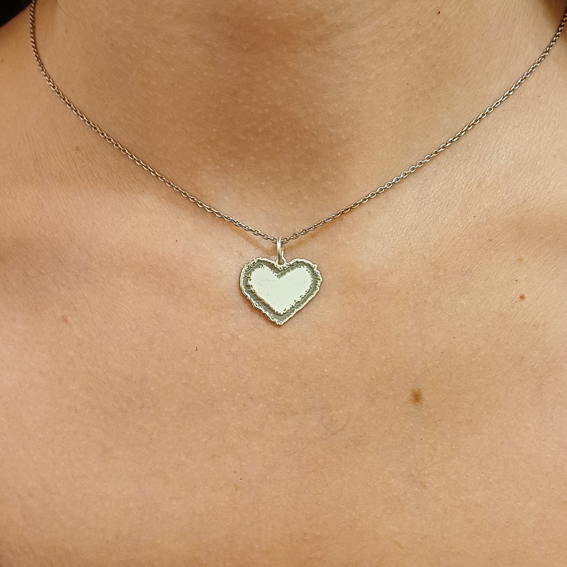 Questo ciondolo è a forma di cuore e realizzato in oro 18 carati. Ha un contorno frastagliato e irregolare, come disegnato a mano libera, con una superficie centrale liscia e morbida al tatto. La forma è piena e il bordo ha una texture ruvida, che lo rende unico e piacevole da accarezzare con le dita. È pensato per essere indossato o saldato su un gioiello, e rappresenta un sentimento puro e vero. Ogni pezzo è fatto a mano nel nostro laboratorio artigianale.
