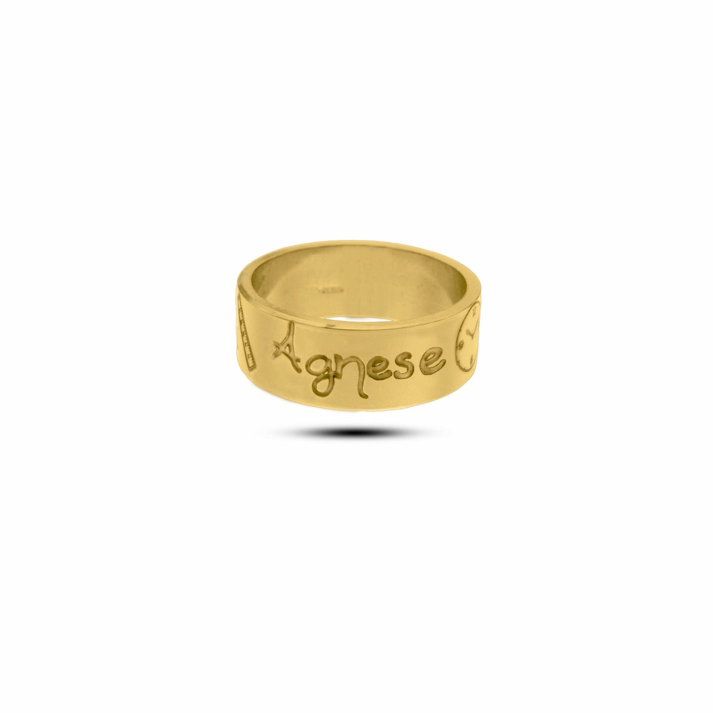L'immagine mostra un anello in oro giallo con una superficie liscia e lucida. Sulla fascia dell'anello sono incisi dei simboli e il nome "Agnese" in uno stile di scrittura a mano. Accanto al nome, c'è un piccolo disegno che rappresenta un righello ,un orologio, un peso ed un calendario tutti con incisi i dati della nascita. L'anello ha un design semplice ma elegante, con incisioni ben definite e dettagli che lo rendono unico 
