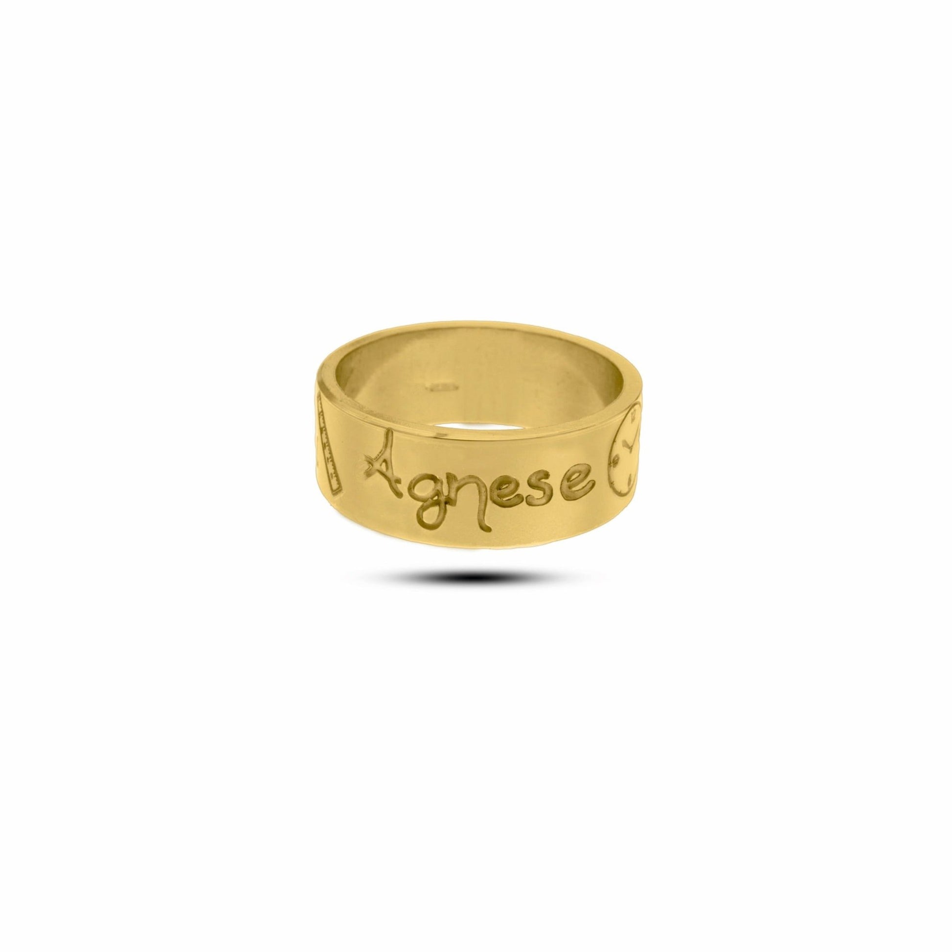 L'immagine mostra un anello in oro giallo con una superficie liscia e lucida. Sulla fascia dell'anello sono incisi dei simboli e il nome "Agnese" in uno stile di scrittura a mano. Accanto al nome, c'è un piccolo disegno che rappresenta un righello ,un orologio, un peso ed un calendario tutti con incisi i dati della nascita. L'anello ha un design semplice ma elegante, con incisioni ben definite e dettagli che lo rendono unico 
