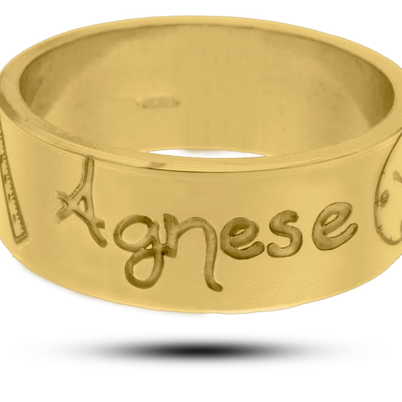 L'immagine mostra un anello in oro giallo con una superficie liscia e lucida. Sulla fascia dell'anello sono incisi dei simboli e il nome "Agnese" in uno stile di scrittura a mano. Accanto al nome, c'è un piccolo disegno che rappresenta un righello ,un orologio, un peso ed un calendario tutti con incisi i dati della nascita. L'anello ha un design semplice ma elegante, con incisioni ben definite e dettagli che lo rendono unico 