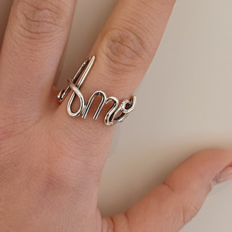 Immagina di accarezzare un filo d’argento liscio e brillante, che si snoda e si intreccia con eleganza fino a formare un nome. È un anello leggero e morbido al tatto, con curve armoniose e una struttura aperta, che segue dolcemente la forma del dito. Ogni lettera è parte di un unico filo, senza interruzioni, donando una sensazione di fluidità e continuità. Un gioiello su misura, pieno di emozione e personalità.