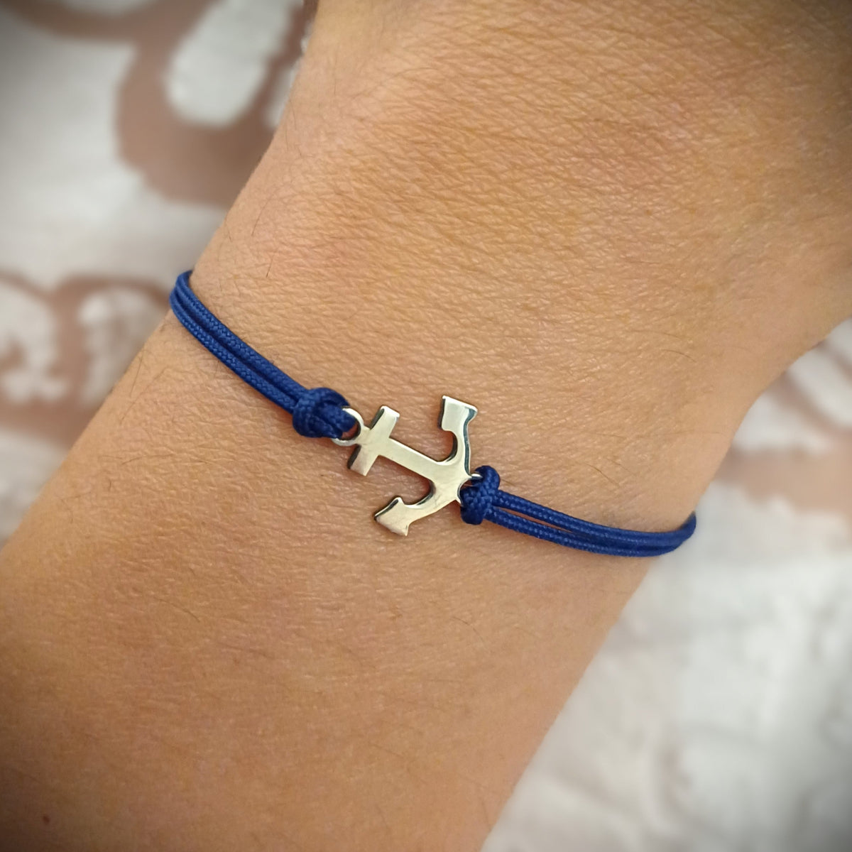 Bracciale ancora in argento 925 con cordino blu indossato al polso
