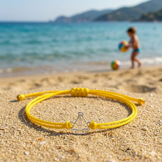 Bracciale con barca a vela in argento 925 e cordino nautico giallo fotografato sulla spiaggia