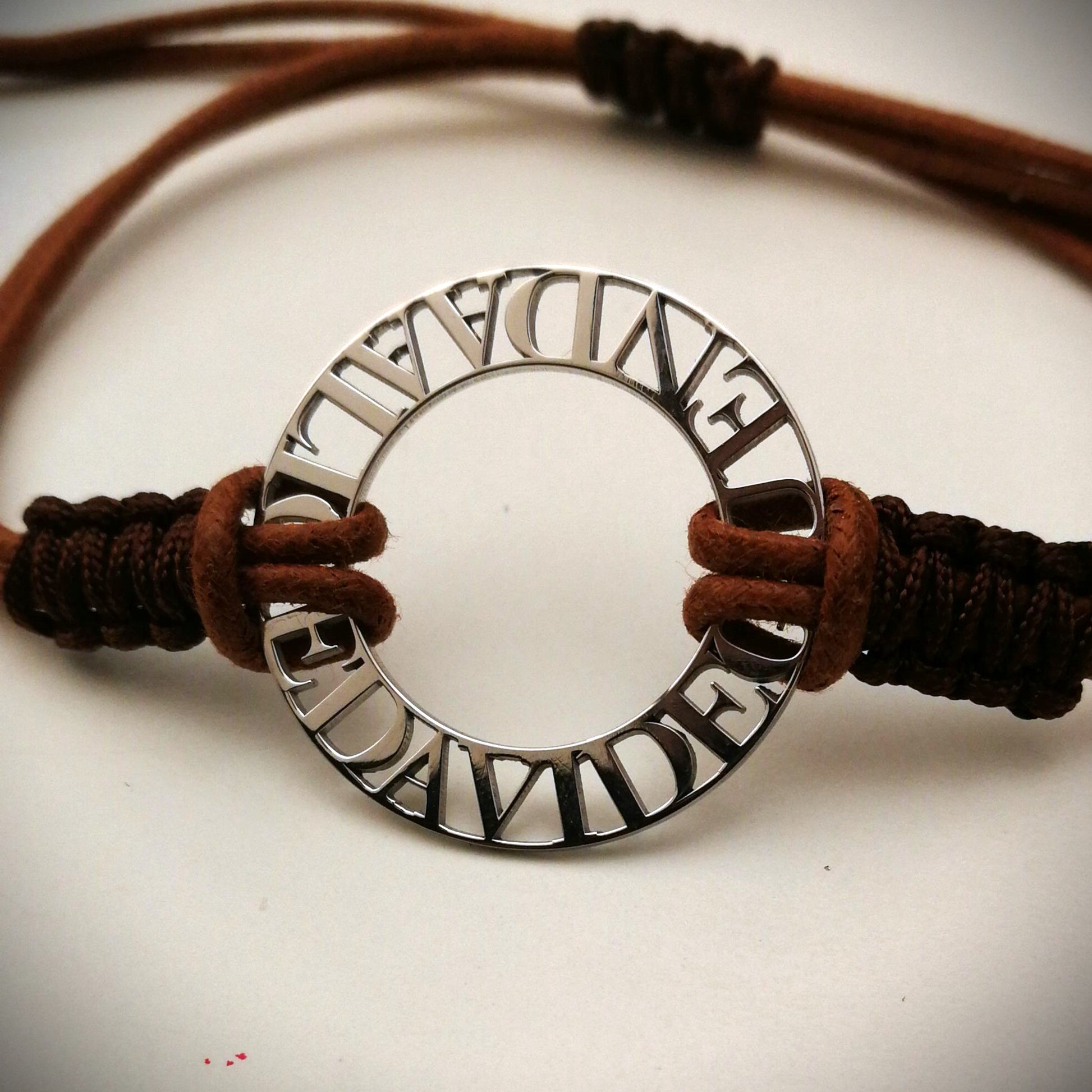 Immagina un cerchio liscio e leggero, con nomi traforati che emergono come piccole sculture tra il vuoto e la luce. Ogni lettera è incisa con precisione, creando un contrasto tra il metallo freddo e il calore del cordino intrecciato a mano, morbido e avvolgente sul polso. La superficie è liscia, con bordi definiti ma delicati al tatto. Questo bracciale personalizzato è un abbraccio in argento, con parole che parlano di affetti, ricordi e connessioni profonde.