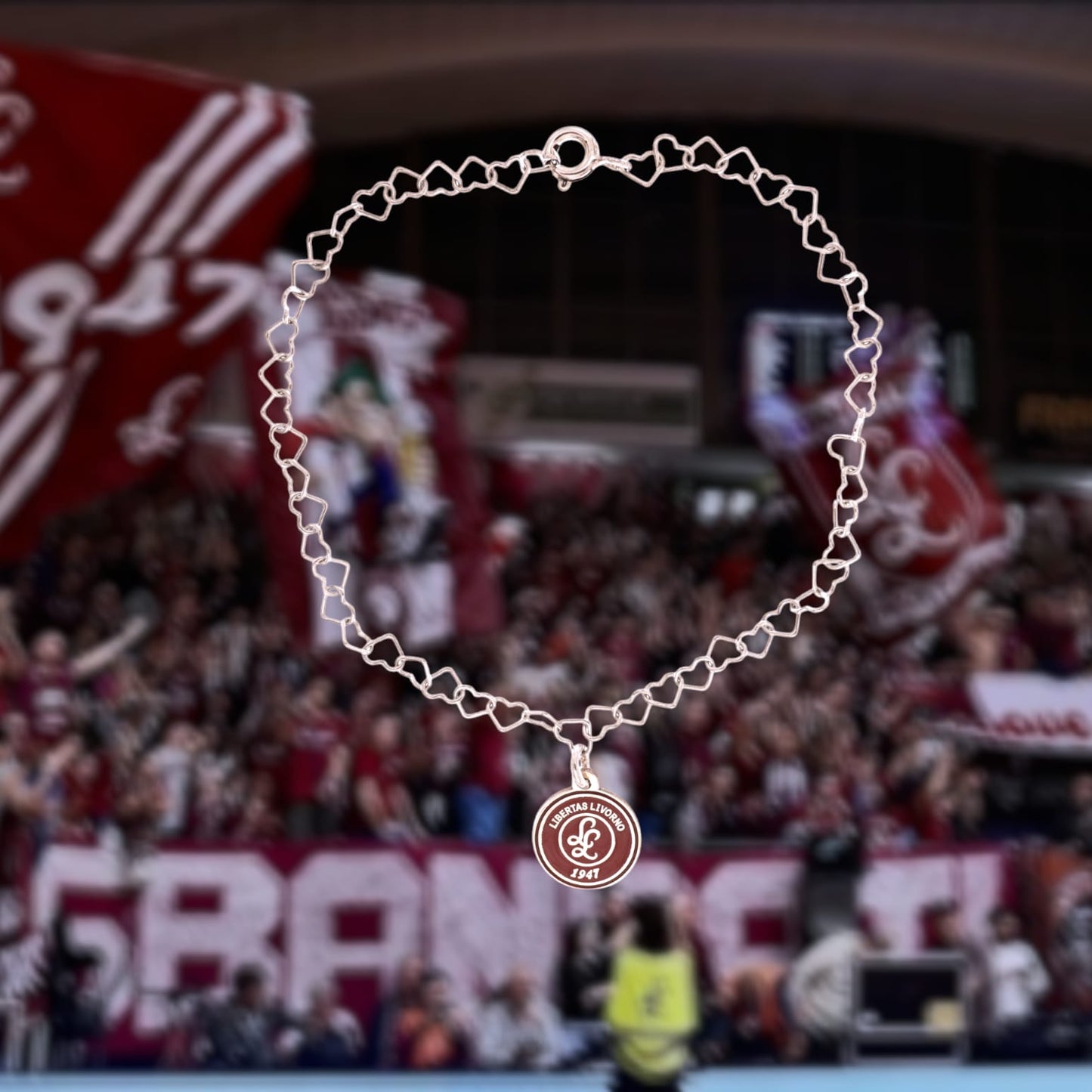 Questo braccialetto in argento 925 ha una catena di maglie a forma di cuore e una medaglietta rotonda da 10 mm. La superficie della medaglietta è lavorata artigianalmente nel nostro laboratorio orafo a Livorno e presenta il logo della Libertas Livorno 1947, inciso a laser e smaltato a caldo con un ricco colore amaranto. È un pezzo elegante e sportivo, pensato per celebrare la passione e l'appartenenza. Ideale per chi cerca gioielli personalizzati e distintivi.