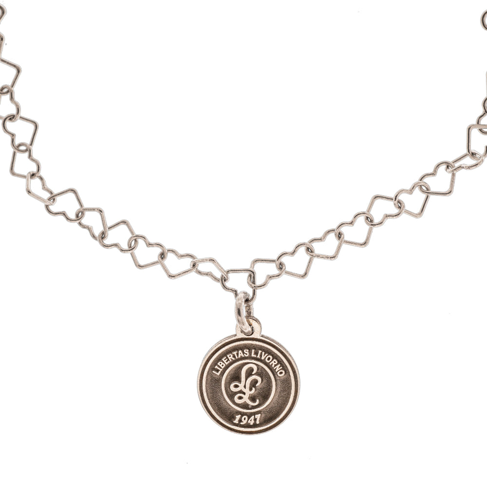 Questo braccialetto in argento 925 ha una catena di maglie a forma di cuore e una medaglietta rotonda da 10 mm. La superficie della medaglietta è lavorata artigianalmente nel nostro laboratorio orafo a Livorno e presenta il logo della Libertas Livorno 1947, inciso a laser e smaltato a caldo con un ricco colore amaranto. È un pezzo elegante e sportivo, pensato per celebrare la passione e l'appartenenza. Ideale per chi cerca gioielli personalizzati e distintivi.