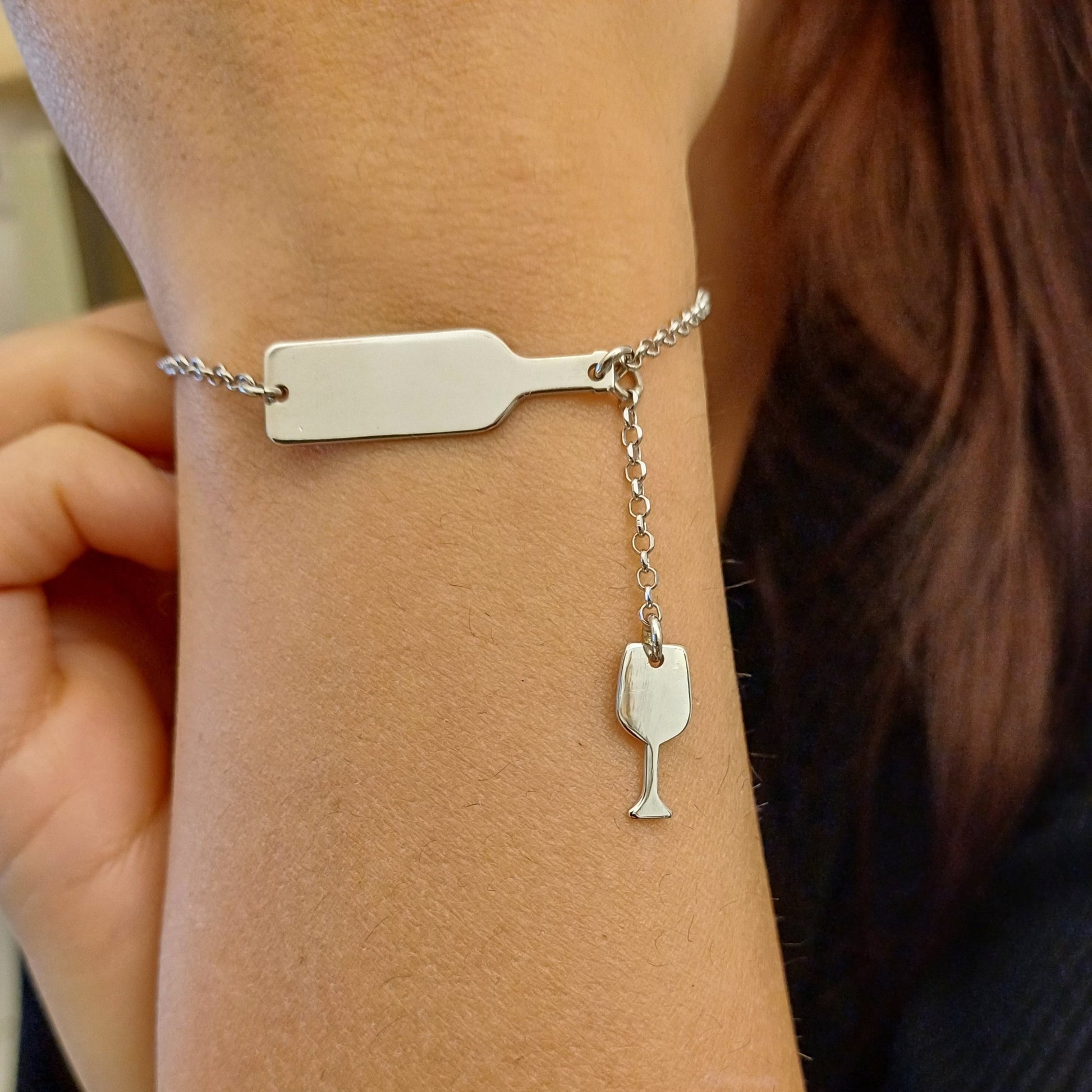 bracciale in argento con un design unico: una bottiglia di vino stilizzata lucida a cui è collegato un piccolo calice pendente. La catenina è sottile a maglie rolò con chiusura a moschettone regolabile, ideale per un look raffinato e originale. Perfetto per gli amanti del vino, questo gioiello aggiunge un tocco di stile e passione al polso. dettaglio indossata