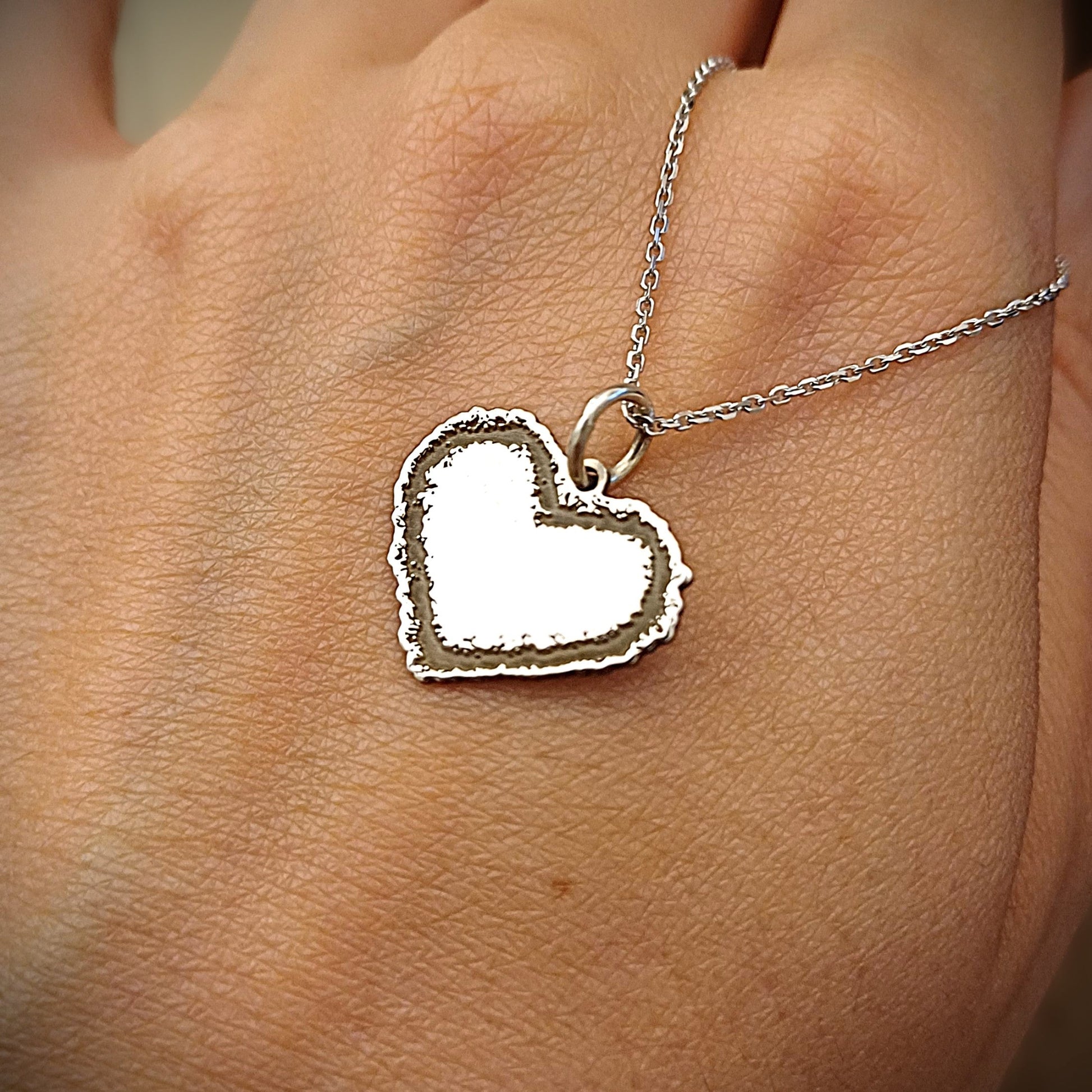 Questo ciondolo è a forma di cuore e realizzato in oro 18 carati. Ha un contorno frastagliato e irregolare, come disegnato a mano libera, con una superficie centrale liscia e morbida al tatto. La forma è piena e il bordo ha una texture ruvida, che lo rende unico e piacevole da accarezzare con le dita. È pensato per essere indossato o saldato su un gioiello, e rappresenta un sentimento puro e vero. Ogni pezzo è fatto a mano nel nostro laboratorio artigianale.