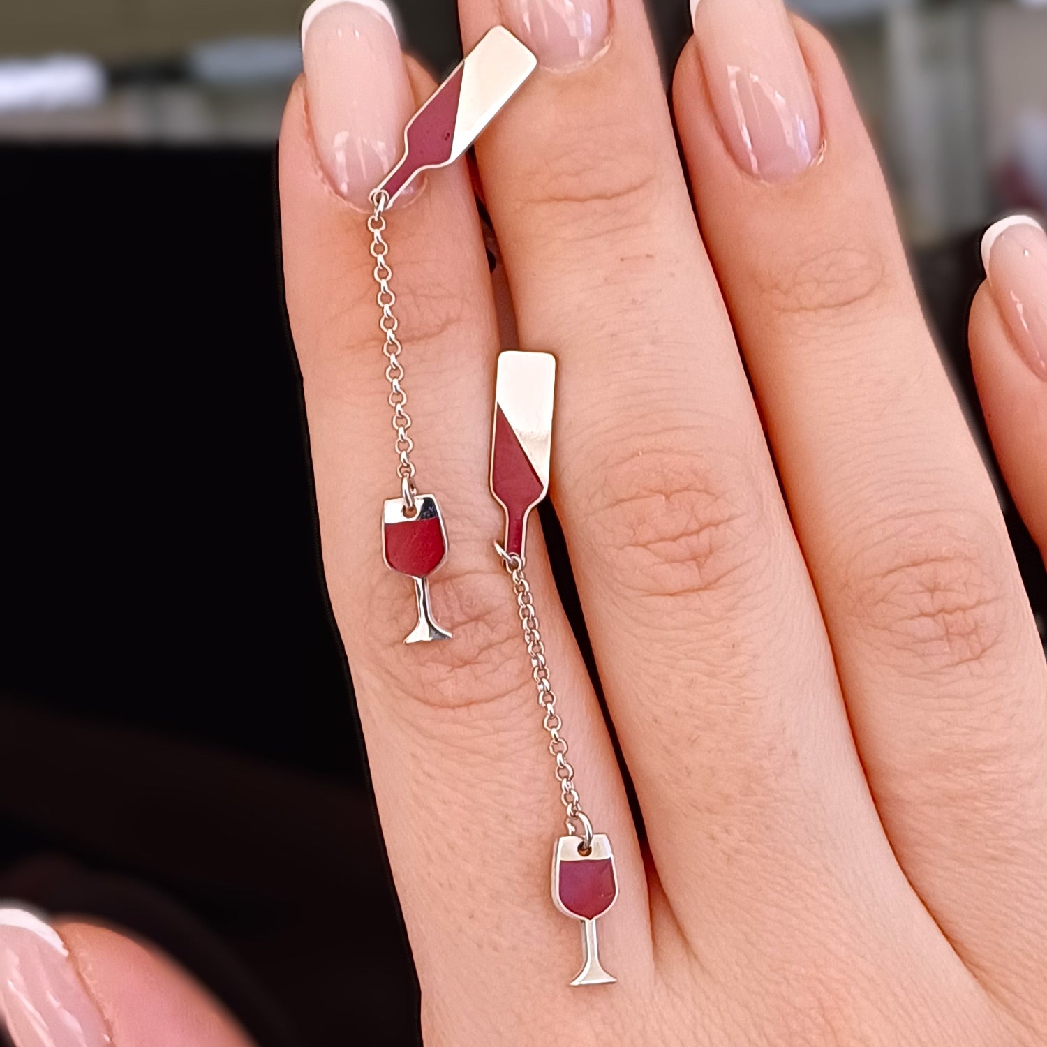Questi orecchini pendenti in argento 925 sono composti da due elementi collegati da una sottile catenella. La parte superiore rappresenta il collo di una bottiglia, mentre il ciondolo inferiore raffigura un calice da vino inclinato, come se stesse versando il suo contenuto. Alcune versioni presentano una smaltatura a caldo in un intenso colore rosso vino. La superficie è incisa al laser, con dettagli ben definiti. Leggeri e lunghi 5 cm, si muovono delicatamente seguendo i movimenti del viso.