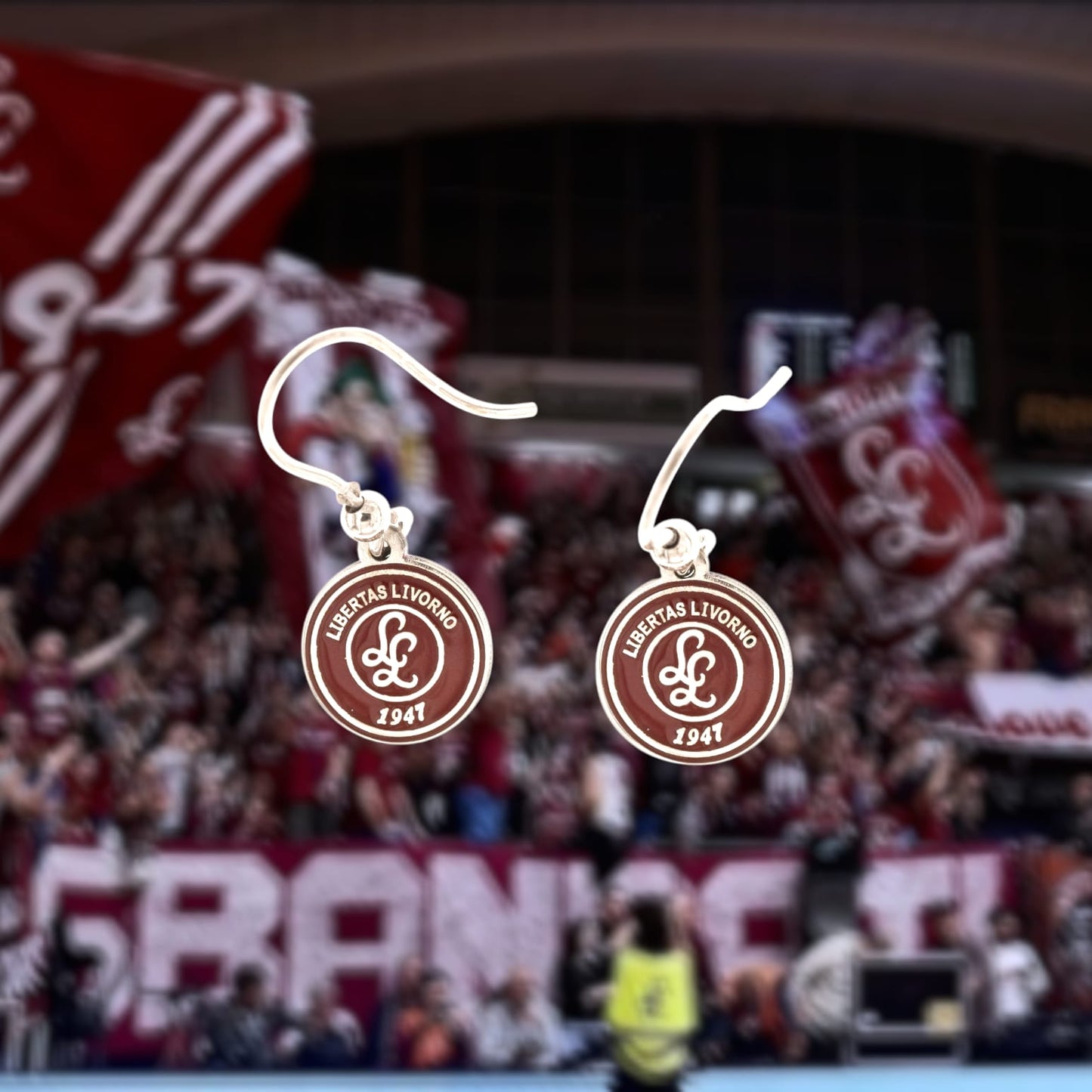 Un paio di orecchini pendenti in argento 925, con un amo elegante e una medaglia da 10 mm, incisa a laser e smaltata in amaranto con il logo della Libertas Livorno 1947. Realizzati artigianalmente nel nostro laboratorio orafo a Livorno, offrono un design raffinato e dettagliato che celebra la passione sportiva. Ideali per chi ama i gioielli personalizzati e desidera indossare un pezzo che racconta la propria appartenenza e amore per il basket