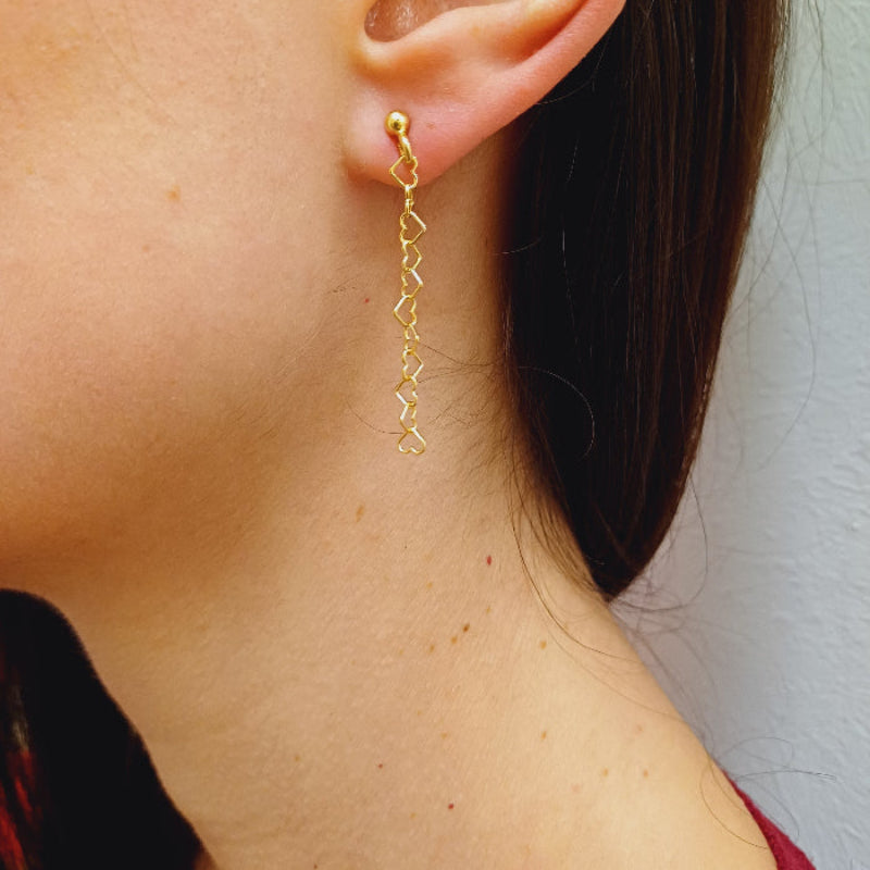 Questi orecchini pendenti sono realizzati in argento 925 nelle varianti Rodiato, Dorato e Ramato e presentano una catena leggera formata da piccoli cuori vuoti collegati tra loro. Il design è arioso e delicato, con una cascata sottile che ondeggia dolcemente con ogni movimento. La chiusura è a perno con farfallina, pratica e sicura. Il colore è un caldo oro giallo lucido, che riflette la luce in modo raffinato. Perfetti per chi ama i dettagli romantici e sofisticati.