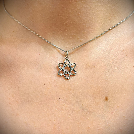 Questo ciondolo rappresenta un atomo stilizzato, con sei orbite che si intrecciano creando una forma armoniosa e simmetrica. È in argento 925, con una finitura mista: liscia e satinata. Al tatto, si percepiscono i cerchi morbidi e leggermente bombati e piccole sfere posizionate lungo le orbite. È leggero, misura 1,4 cm di altezza ed è piatto, ma con rilievi netti che lo rendono facile da riconoscere anche solo con le dita.