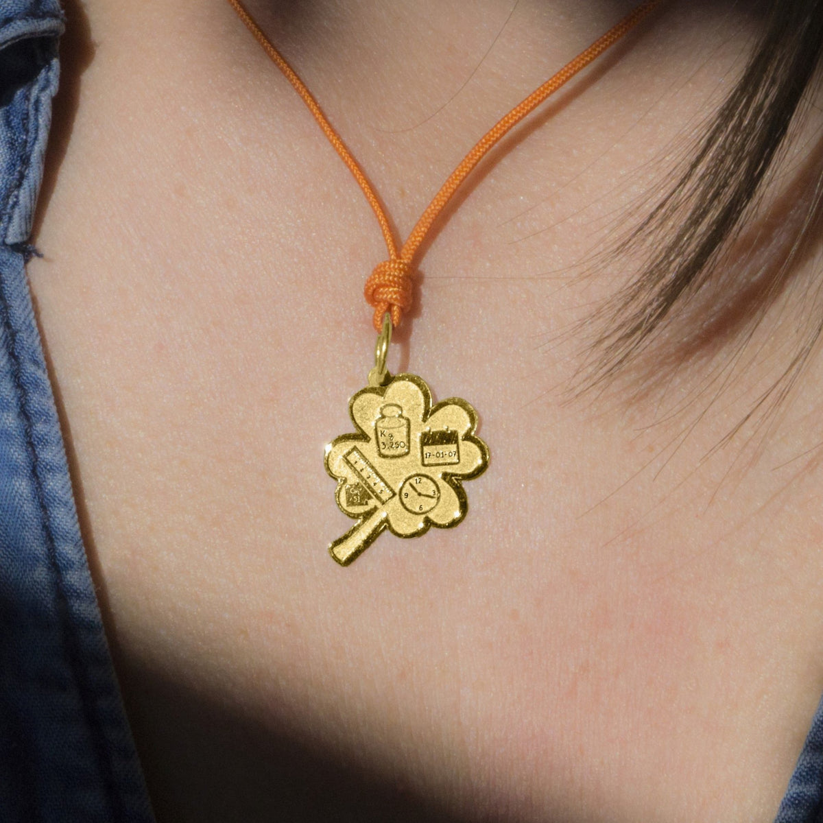 Pendente Quadrifoglio Nascita personalizzato in oro indossato con cordino arancio