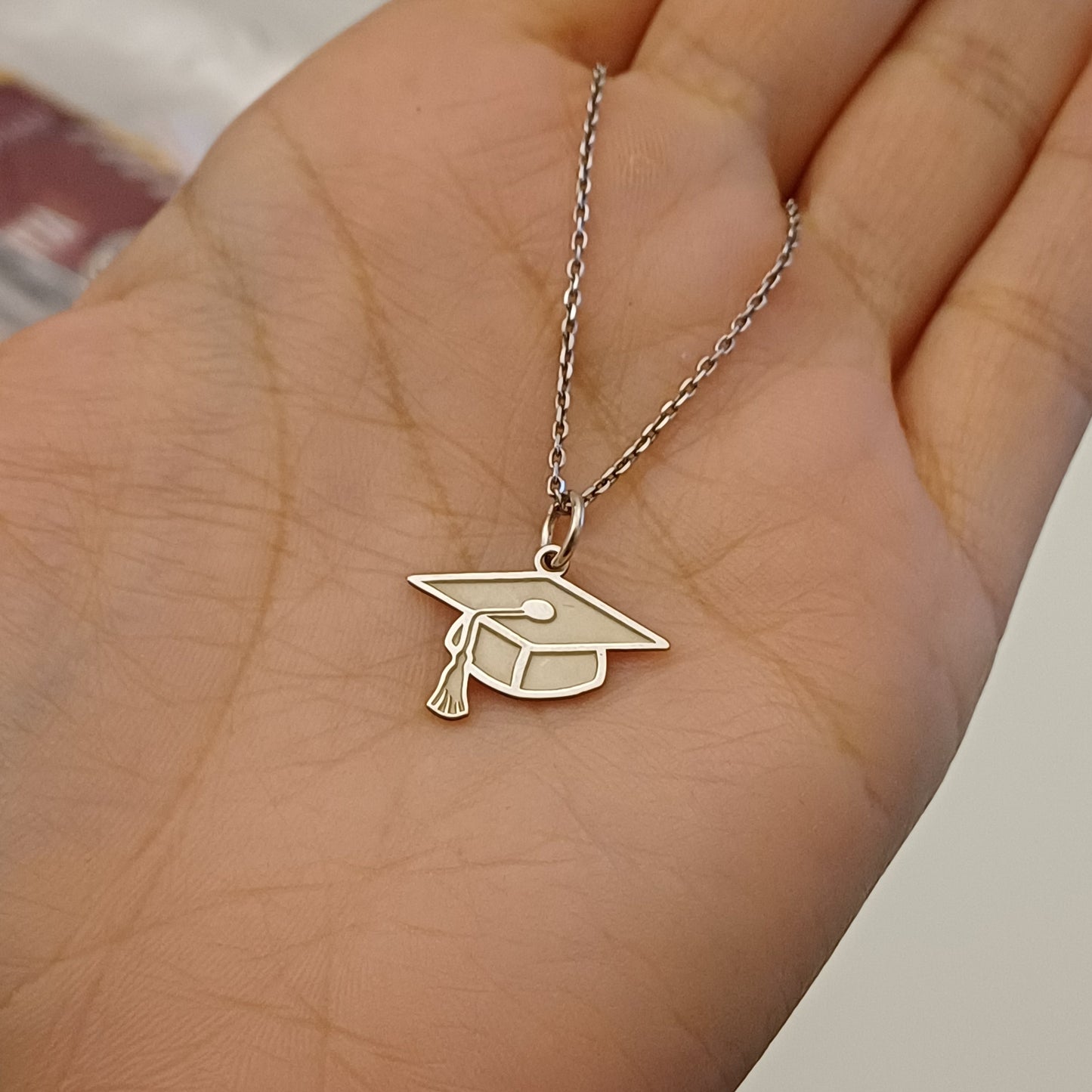 Pendente a forma di cappello di laurea in rilievo, realizzato a mano e alto 14 mm. Disponibile in oro giallo, oro bianco o argento 925. Ha una finitura satinata sul fronte e un retro lucido, ideale per incisioni personalizzate. Un gioiello simbolico che celebra un importante traguardo con eleganza e significato.