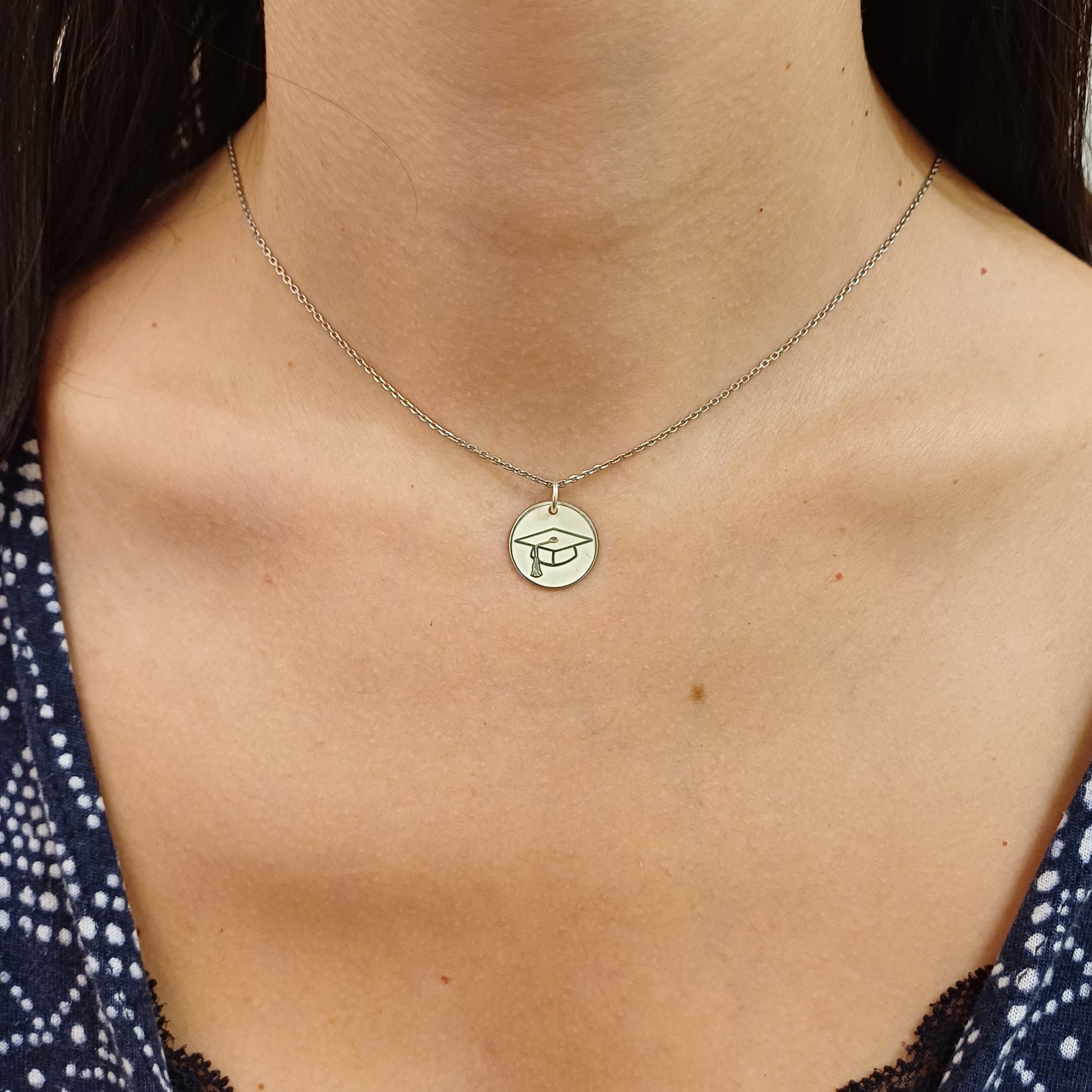 Pendente tondo da 15 mm, realizzato a mano, disponibile in oro giallo, oro bianco o argento 925. Sul fronte, una finitura satinata con cappello di laurea in rilievo; sul retro, superficie lucida perfetta per un'incisione personalizzata. Un gioiello simbolico, da regalare a chi ha raggiunto un importante traguardo accademico.
