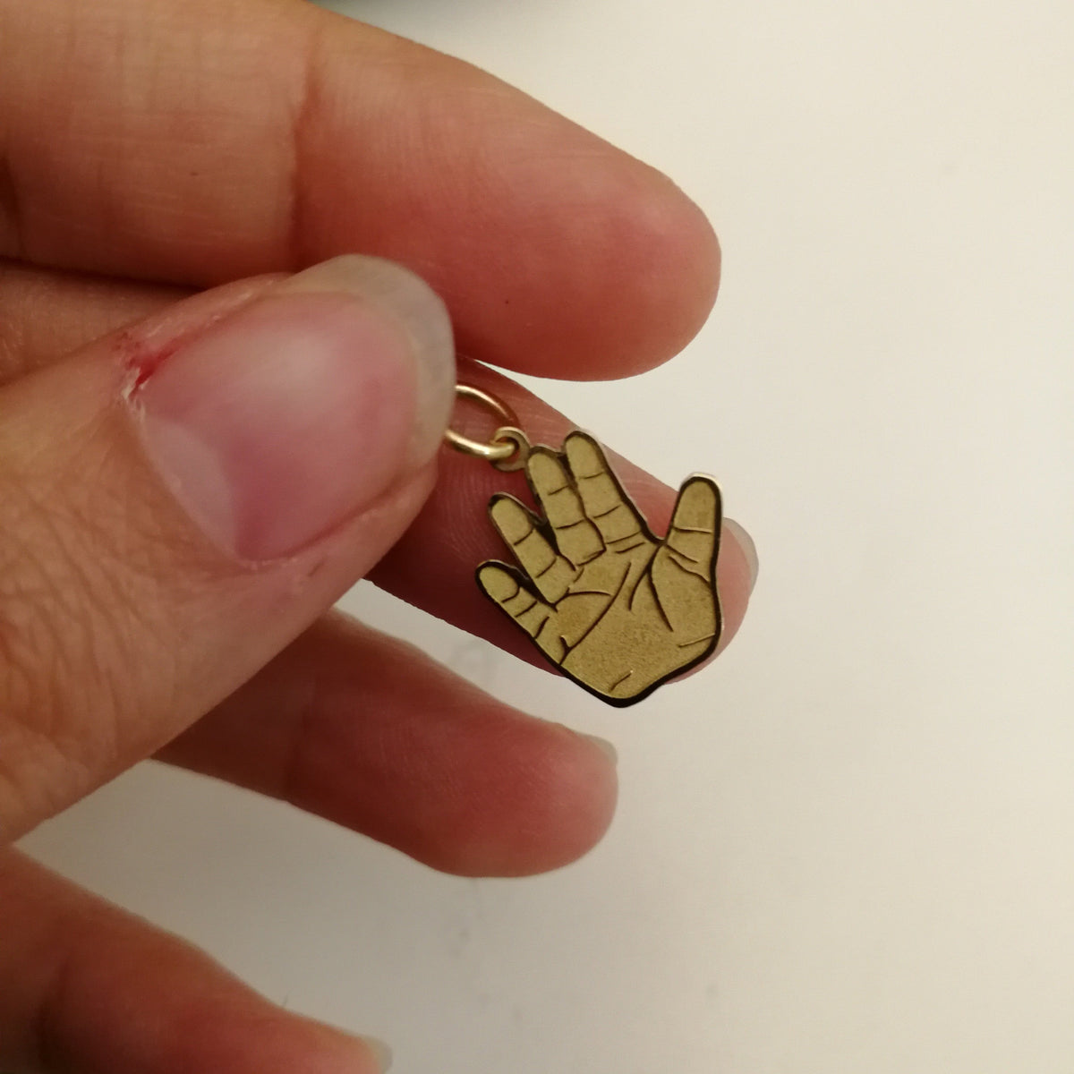 Pendente a forma di mano in oro tenuto tra le dita, con dettaglio ravvicinato delle linee del palmo, anellino superiore e proporzione reale del ciondolo da 15 mm
