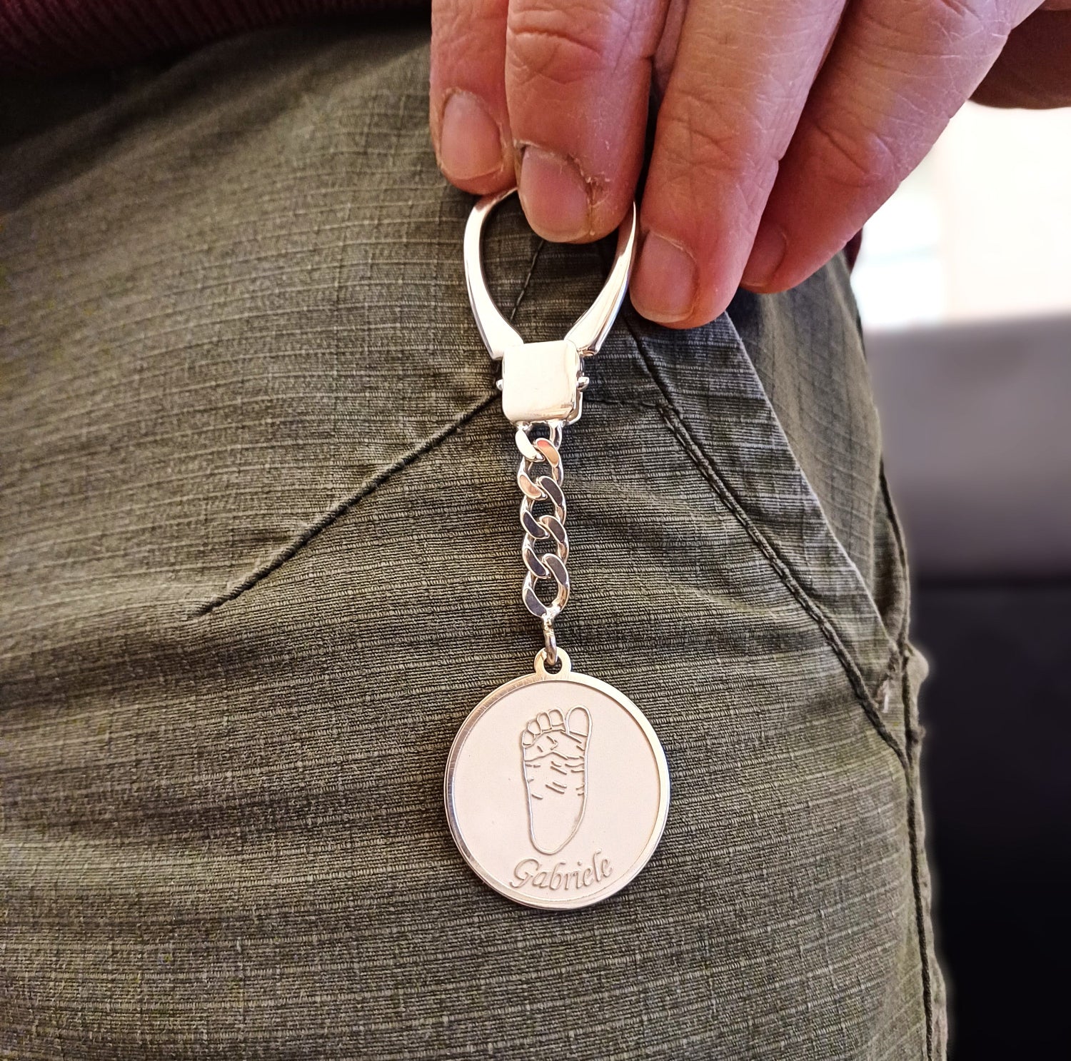 Il portachiavi in argento 925 è un gioiello speciale, inciso a laser con l'impronta della mano di un bambino. L'incisione nasce da una foto, trasformata in un dettaglio scolpito su una medaglia lucente. La superficie è liscia e brillante, con dettagli in rilievo che evocano affetto e personalità. Realizzato in un laboratorio orafo a Livorno, questo portachiavi appartiene alla linea Gioielli Baby, rendendolo un accessorio prezioso e unico