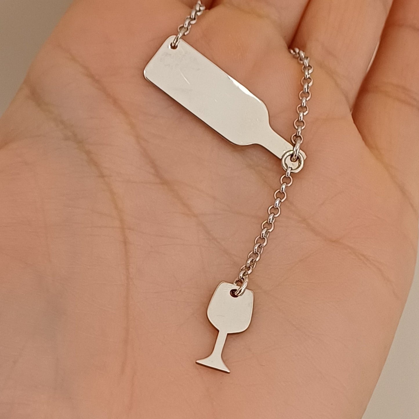 Questo girocollo è realizzato a mano nel nostro laboratorio orafo a Livorno in argento 925. La catenina sottile sostiene due ciondoli lucidi: una bottiglia inclinata e un bicchiere appeso sotto di essa. Il design è minimalista, con superfici lisce e dettagli semplici, che richiamano l'amore per il vino in modo elegante e discreto. La bottiglia e il bicchiere hanno una finitura lucida, che dona brillantezza al gioiello. È possibile personalizzare il girocollo con un'incisione Laser