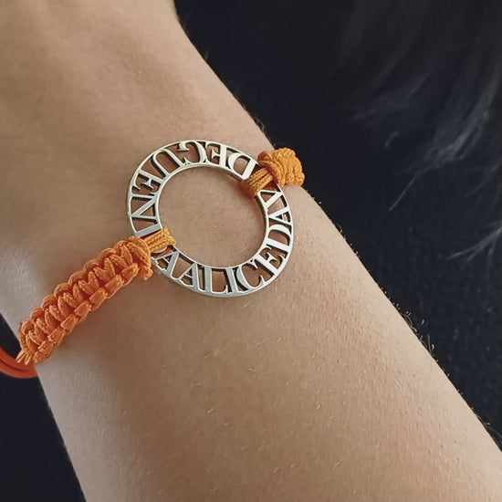 Immagina un cerchio liscio e leggero, con nomi traforati che emergono come piccole sculture tra il vuoto e la luce. Ogni lettera è incisa con precisione, creando un contrasto tra il metallo freddo e il calore del cordino intrecciato a mano, morbido e avvolgente sul polso. La superficie è liscia, con bordi definiti ma delicati al tatto. Questo bracciale personalizzato è un abbraccio in argento, con parole che parlano di affetti, ricordi e connessioni profonde.