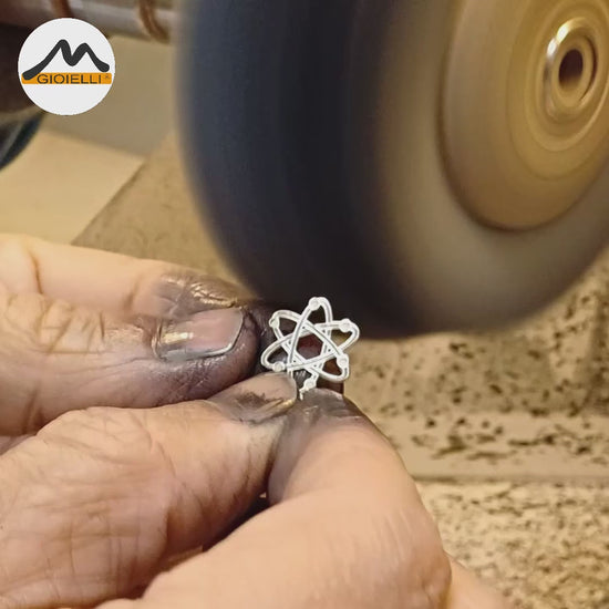 Questo ciondolo rappresenta un atomo stilizzato, con sei orbite che si intrecciano creando una forma armoniosa e simmetrica. È in argento 925, con una finitura mista: liscia e satinata. Al tatto, si percepiscono i cerchi morbidi e leggermente bombati e piccole sfere posizionate lungo le orbite. È leggero, misura 1,4 cm di altezza ed è piatto, ma con rilievi netti che lo rendono facile da riconoscere anche solo con le dita.