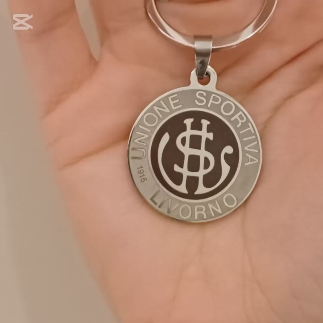 Questo portachiavi in acciaio dal diametro di 30 mm è robusto ma leggero, con una superficie liscia e fresca al tatto. Sul fronte, l’incisione laser del logo dell’U.S. Livorno crea un leggero rilievo percepibile con i polpastrelli, mentre il retro è personalizzabile con un’incisione su richiesta. Il metallo ha una finitura opaca ma riflettente, resistente all’usura. Pensato per i veri tifosi, è un oggetto elegante e simbolico, perfetto da portare sempre con sé.