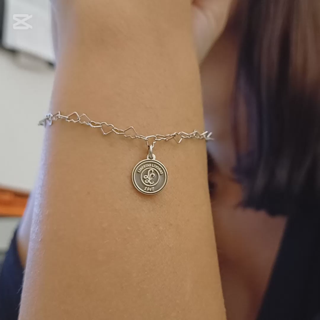 Questo braccialetto in argento 925 ha una catena di maglie a forma di cuore e una medaglietta rotonda da 10 mm. La superficie della medaglietta è lavorata artigianalmente nel nostro laboratorio orafo a Livorno e presenta il logo della Libertas Livorno 1947, inciso a laser e smaltato a caldo con un ricco colore amaranto. È un pezzo elegante e sportivo, pensato per celebrare la passione e l'appartenenza. Ideale per chi cerca gioielli personalizzati e distintivi.