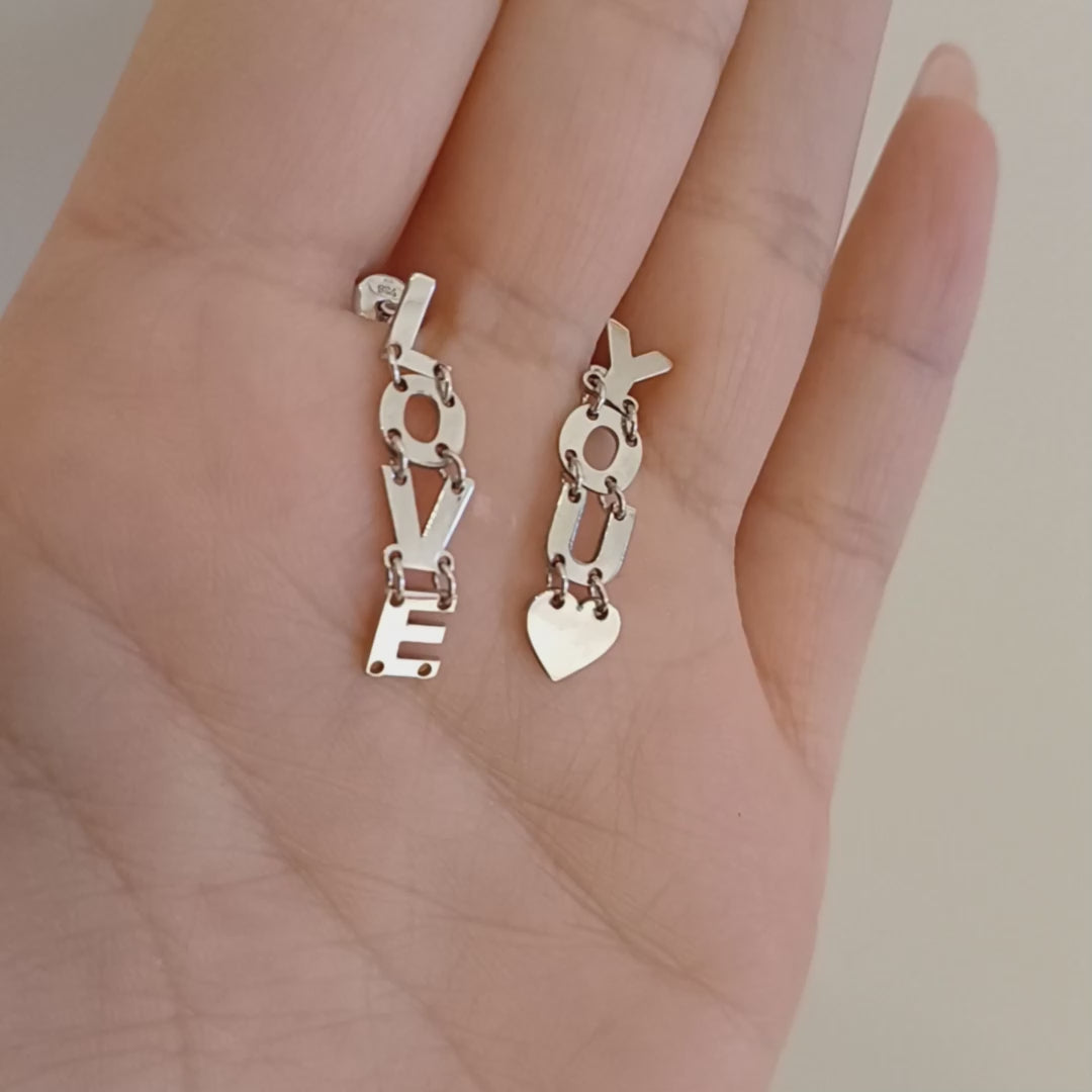 Gli orecchini sono pendenti e mobili, composti da lettere snodabili che formano la scritta "I LOVE YOU". Sono realizzati in argento liscio e brillante, con un design elegante e leggero. Grazie ai piccoli snodi tra le lettere, si muovono delicatamente ad ogni passo, creando un effetto dinamico e raffinato. Perfetti per chi ama gioielli con significato, esprimono un messaggio romantico e universale, da indossare con leggerezza e stile.