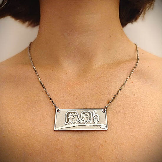 Girocollo in argento 925, con catena fine e leggera.
Al centro pende una targhetta piatta e lucida, grande circa 2,5 cm, di forma rettangolare.
Sulla superficie è inciso il disegno di un bambino, spesso fatto a mano su carta e poi fedelmente riportato sul metallo.
Il bordo è morbido e leggermente stondato, il tutto è liscio al tatto.
Il girocollo è leggero, con chiusura semplice e sicura. Si porta vicino al cuore.