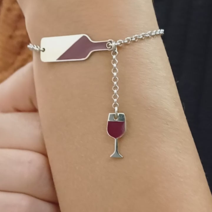  bracciale in argento con un design unico: una bottiglia di vino stilizzata smaltata di rosso, a cui è collegato un piccolo calice pendente. La bottiglia, smaltata obliqua, ricorda il vino mentre si versa, il calice completa il tema con eleganza. La catenina è sottile, con chiusura a moschettone regolabile, ideale per un look raffinato e originale. Perfetto per gli amanti del vino, questo gioiello aggiunge un tocco di stile e passione al polso. video dettaglio indossato