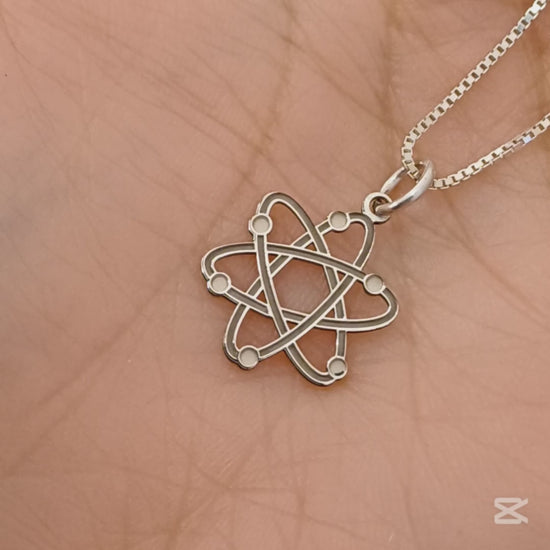 Questo ciondolo rappresenta un atomo stilizzato, con sei orbite che si intrecciano creando una forma armoniosa e simmetrica. È in argento 925, con una finitura mista: liscia e satinata. Al tatto, si percepiscono i cerchi morbidi e leggermente bombati e piccole sfere posizionate lungo le orbite. È leggero, misura 1,4 cm di altezza ed è piatto, ma con rilievi netti che lo rendono facile da riconoscere anche solo con le dita.