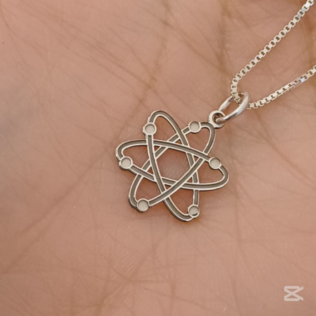 Questo ciondolo rappresenta un atomo stilizzato, con sei orbite che si intrecciano creando una forma armoniosa e simmetrica. È in argento 925, con una finitura mista: liscia e satinata. Al tatto, si percepiscono i cerchi morbidi e leggermente bombati e piccole sfere posizionate lungo le orbite. È leggero, misura 1,4 cm di altezza ed è piatto, ma con rilievi netti che lo rendono facile da riconoscere anche solo con le dita.