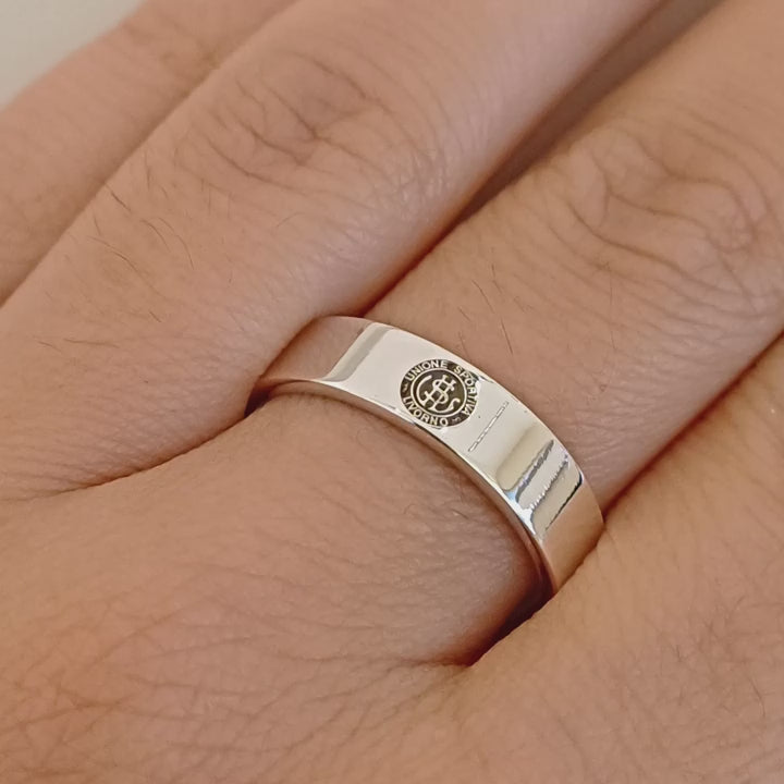 Immaginati un anello dalla forma semplice e robusta. La sua fascia, larga 5  millimetri, avvolge il dito con un tocco deciso. La superficie, liscia e lucida, è interrotta da un'incisione smaltata: il logo dell'U.S. Livorno. Un gioiello realizzato a mano nel nostro laboratorio orafo, perfetto per chi vuole mostrare con orgoglio la propria passione per i colori amaranto. Un pezzo unico, personalizzabile e resistente, creato appositamente per te.